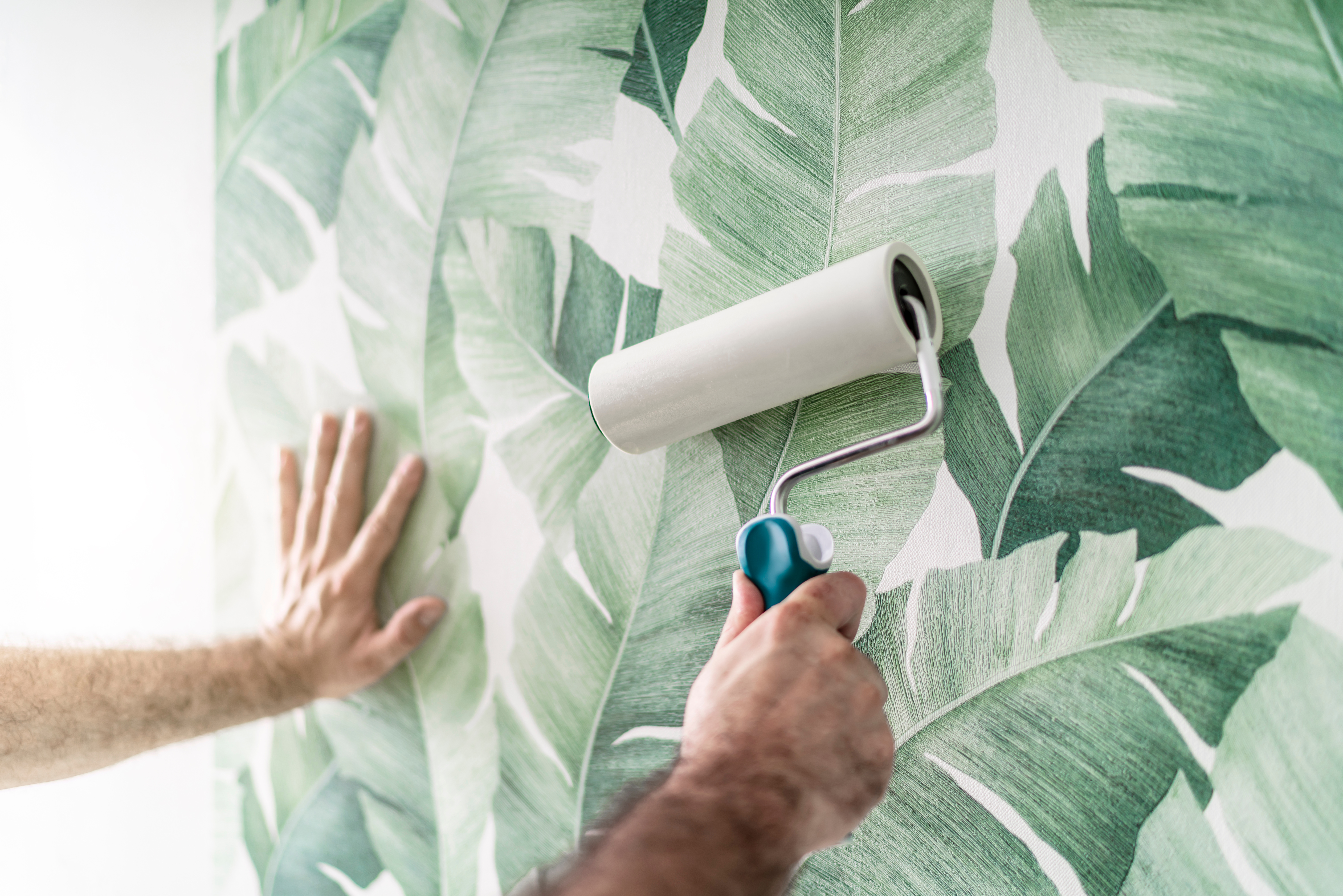 Tapezierer drückt die frisch verklebte Mustertapete mit der Rolle an die Wand